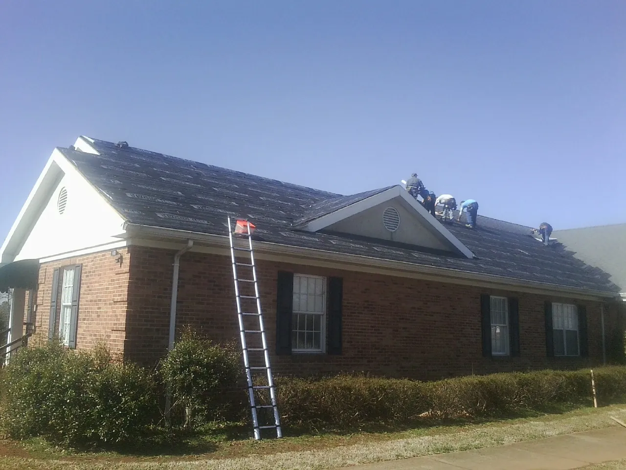 Crew tearing shingles off a brick ranch roof with a ladder set — Emergency Roof Repair work by our crew in Skaneateles Falls