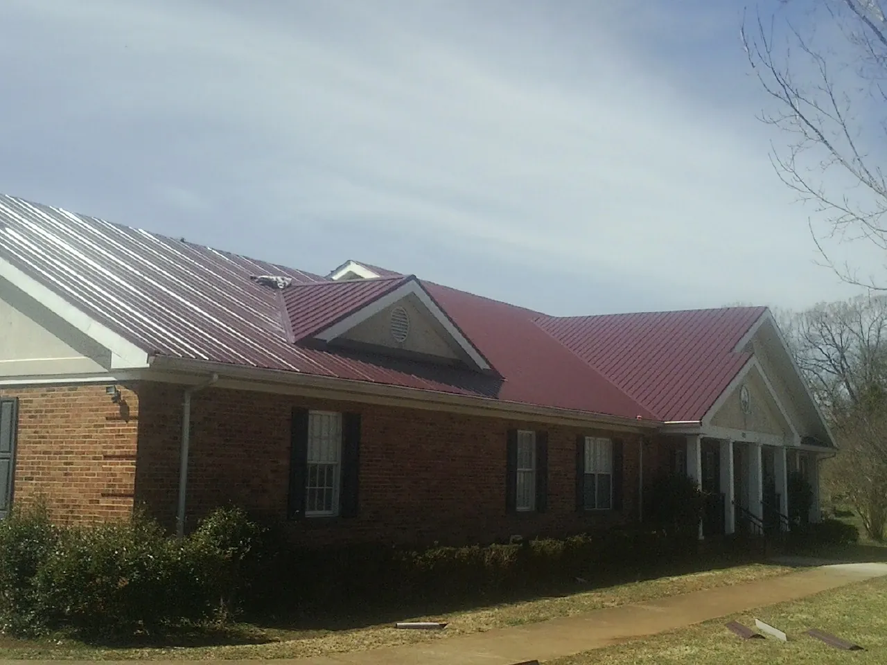 Red metal roof with gabled entries on a long brick building, from a Hail Damage Roof Repair job in Skaneateles Falls
