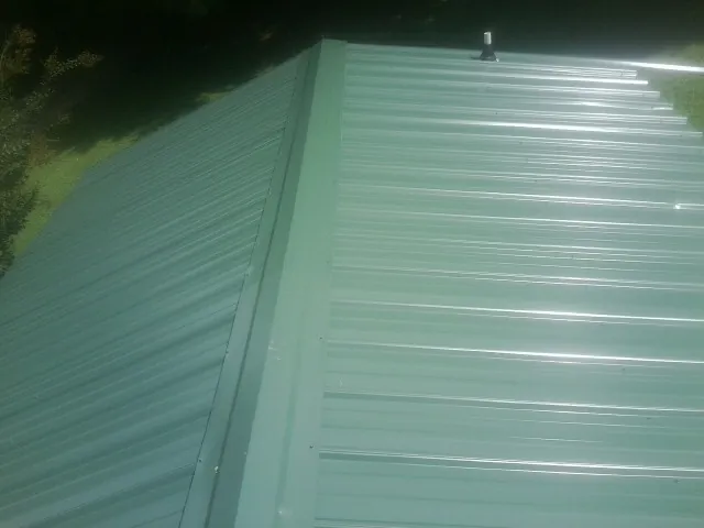 New green metal panels meeting at the ridge of a roof — Flat Roof Repair work by our crew in Skaneateles Falls