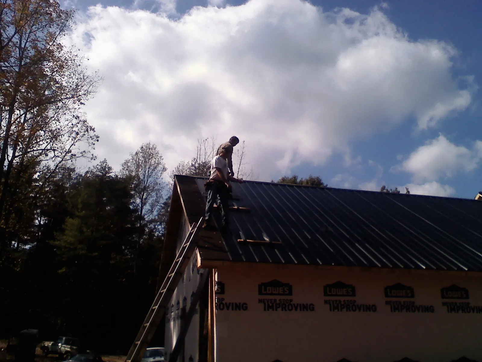 Roofer fastening dark metal panels high against a cloudy sky, from a Roof Inspection job in Skaneateles Falls