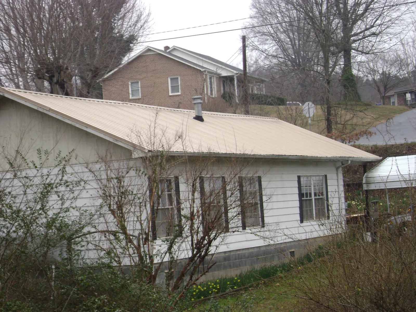 Tan metal roof on a white sided house set into a hillside — Commercial Roofing by Roofing Brothers in Skaneateles Falls