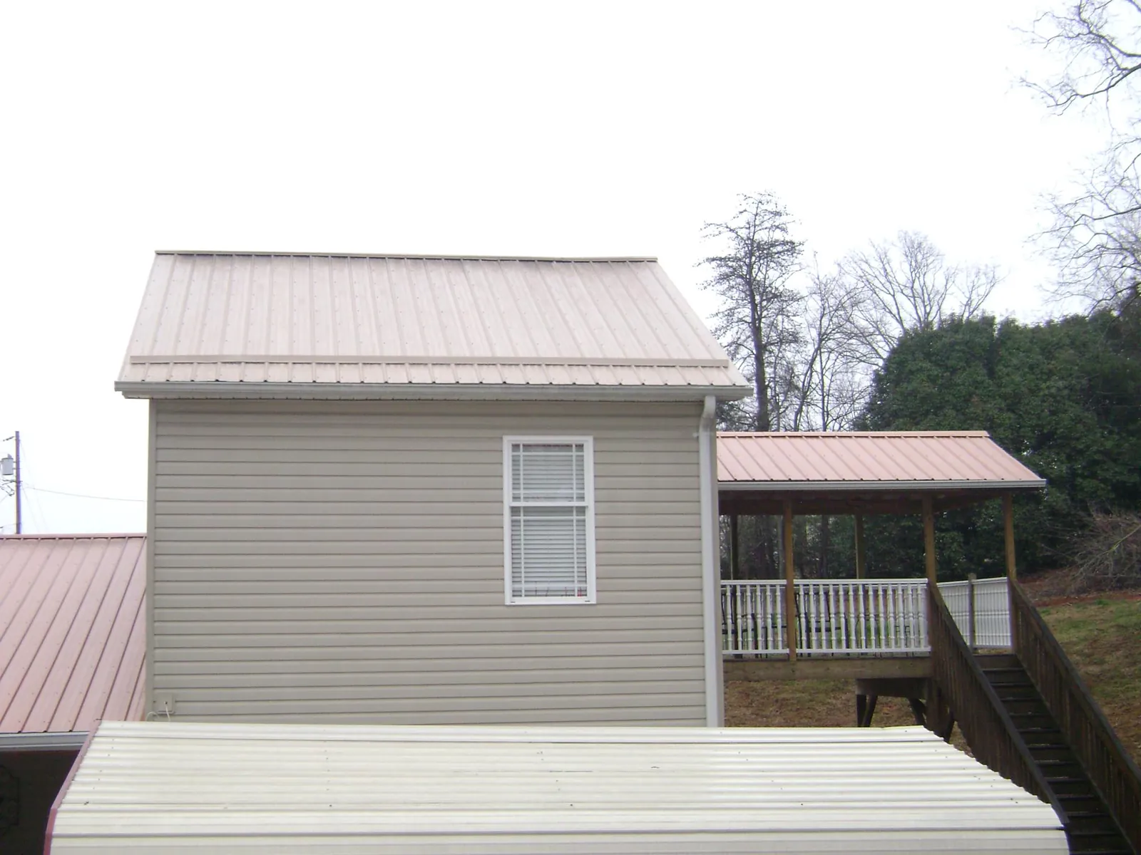 Tan metal roofs on a two story addition and attached porch, from a Roof Replacement job in Skaneateles Falls